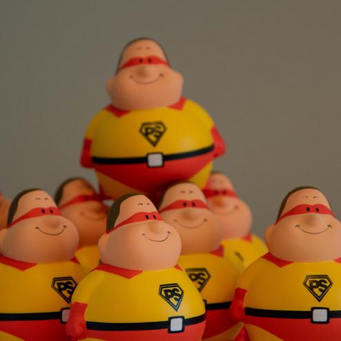 Mehrere rot-gelbe Spielzeugfiguren mit lächelnden Gesichtern und einem Logo auf der Brust, aufgereiht in einer Gruppe.